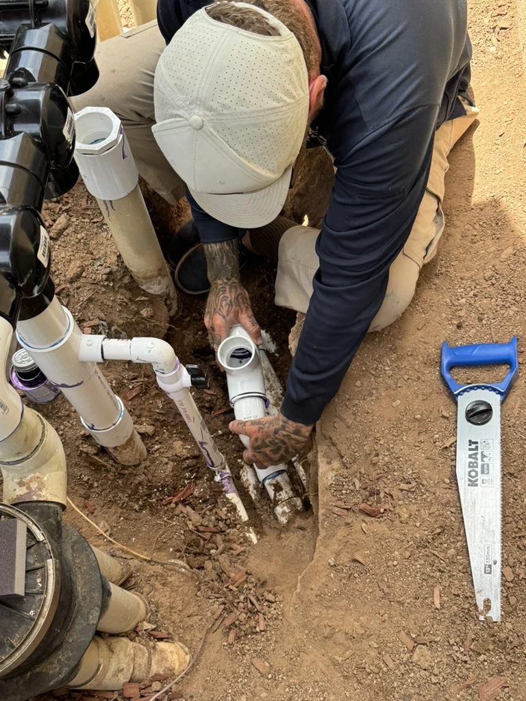 Technician positioning a PVC fitting in exposed underground pool plumbing