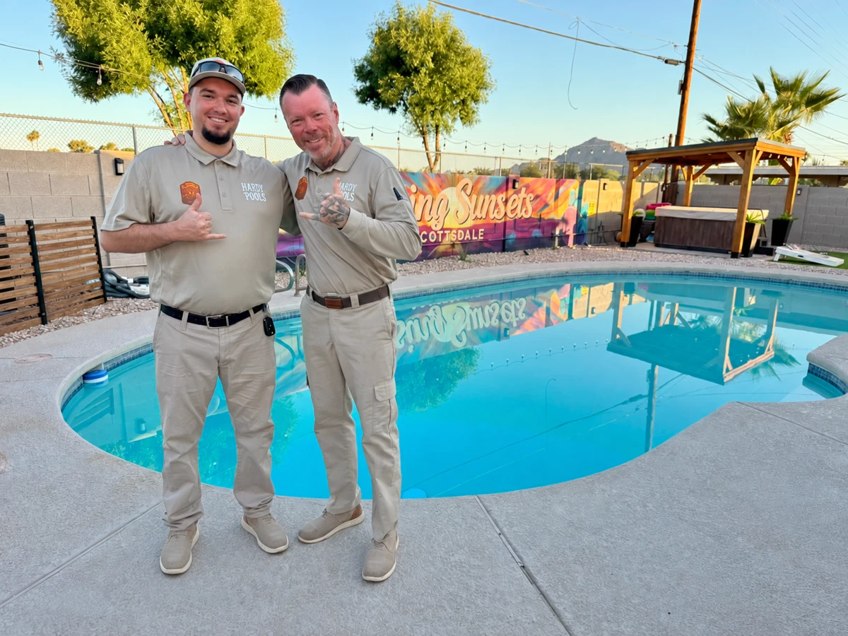 Tyler and Paule smiling and making shaka gestures beside a pool