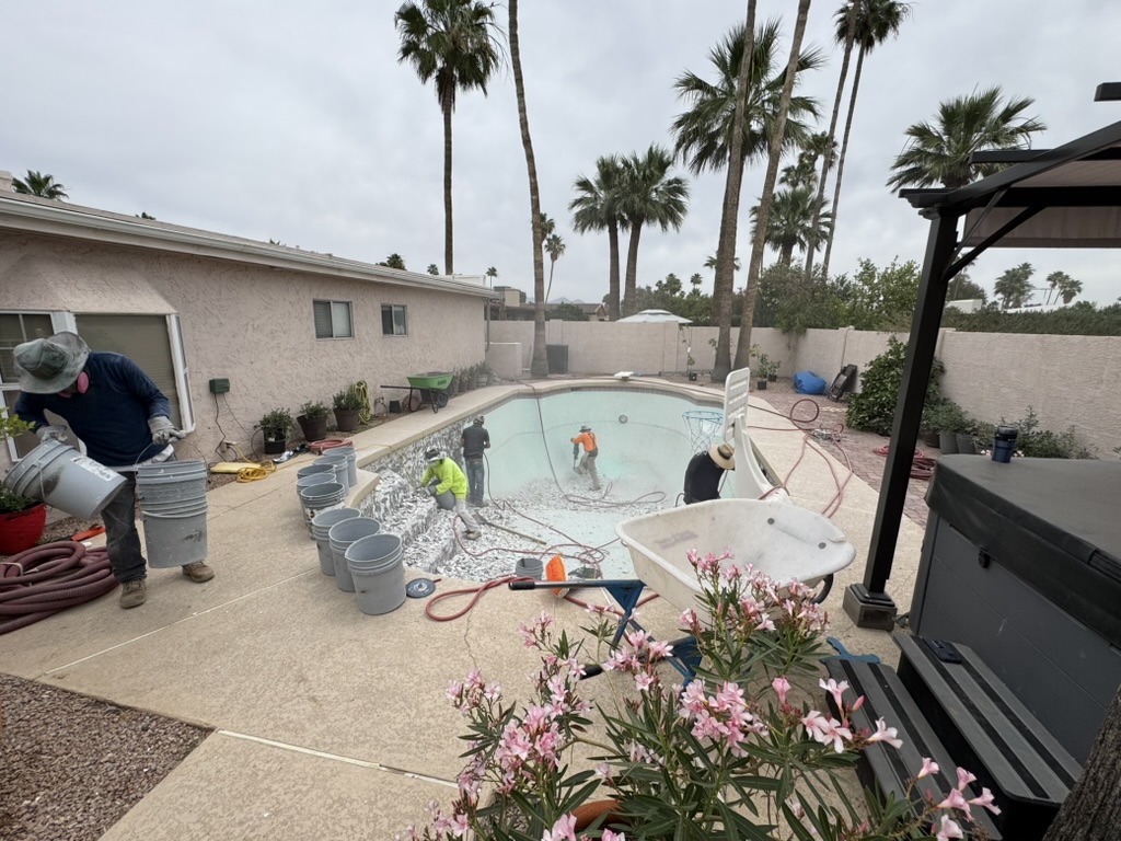 Crew chipping out the old pool finish, with rubble, buckets, hoses and a wheelbarrow around the drained pool