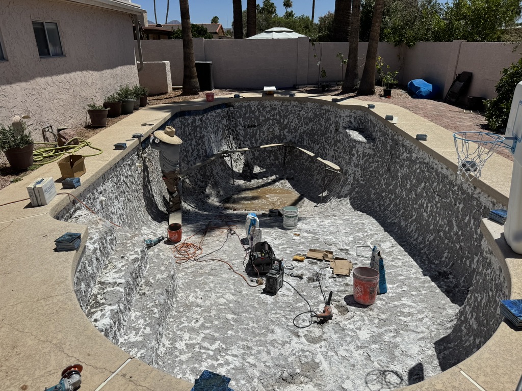 The stripped pool interior during preparation, with a worker and tools in the drained basin.