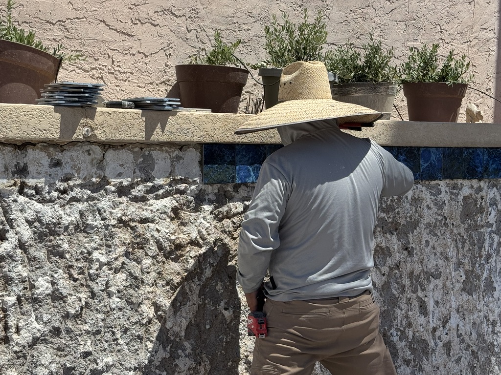 The mason installing blue tile along the pool’s waterline.